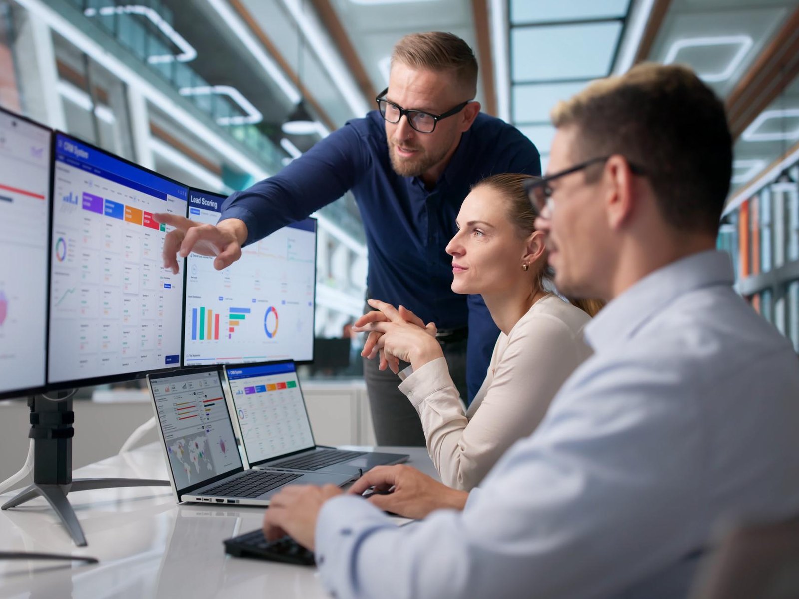 A team reviewing CRM dashboards across monitors and laptops in an open-plan office